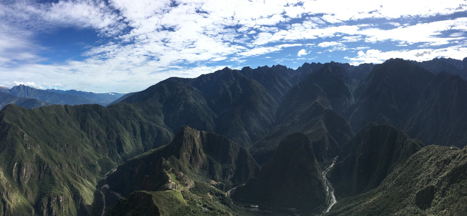 Machu Picchu vu depuis la Montaña, panorama complet sur les montagnes andines et la vallée encaissée sous un ciel bleu nuageu