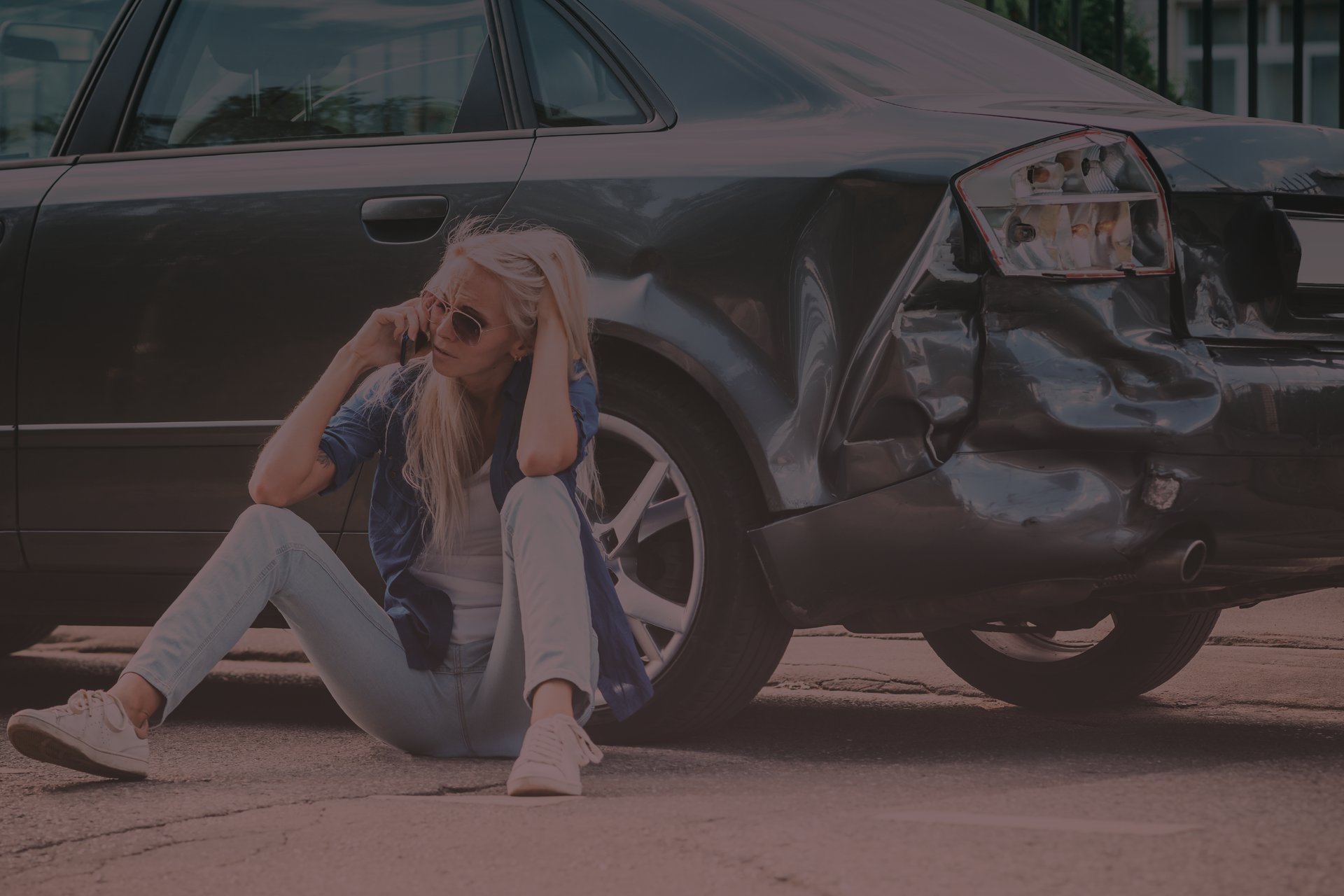 mujer llamando desde celular apoyada en auto chocado