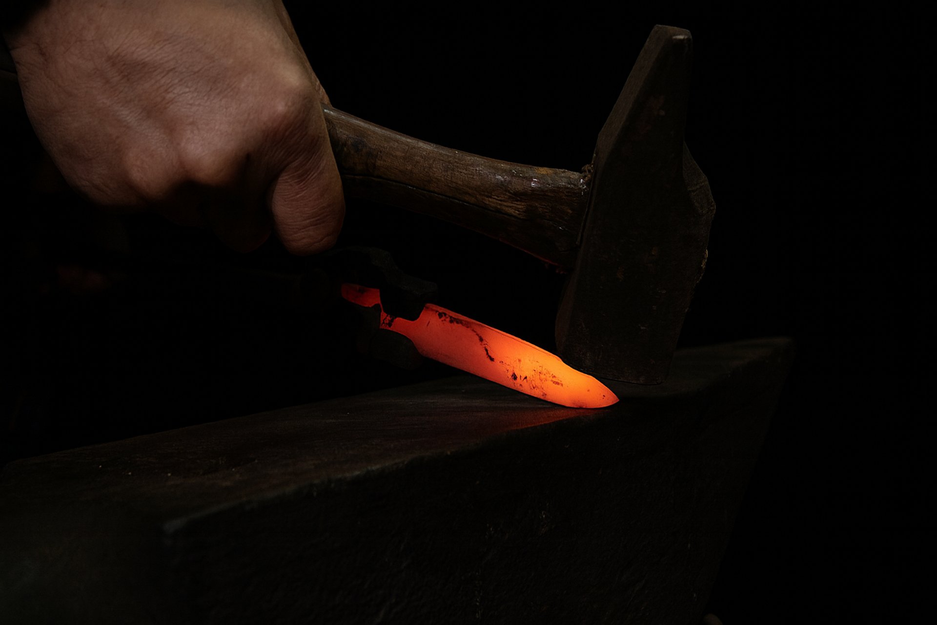 man pounding hammer on hot iron rod