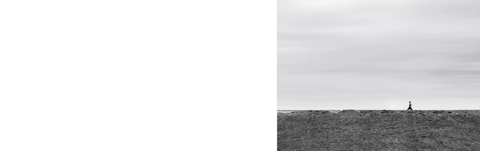A lonely person in a greay daytime walking a a road with the sky in the background