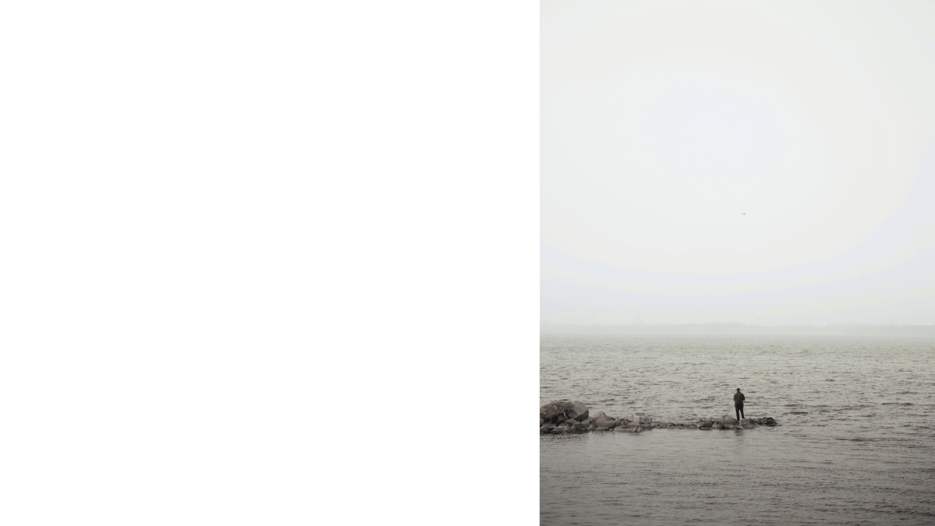 A lonely person standing fishing on a large stone pier