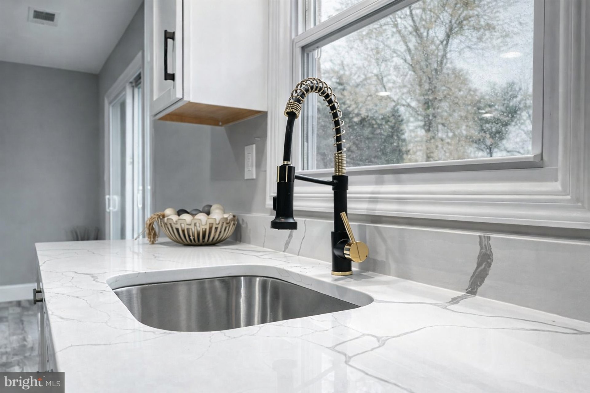 Modern kitchen undermount sink with black and gold coil spring faucet, white quartz marble countertop, and natural light