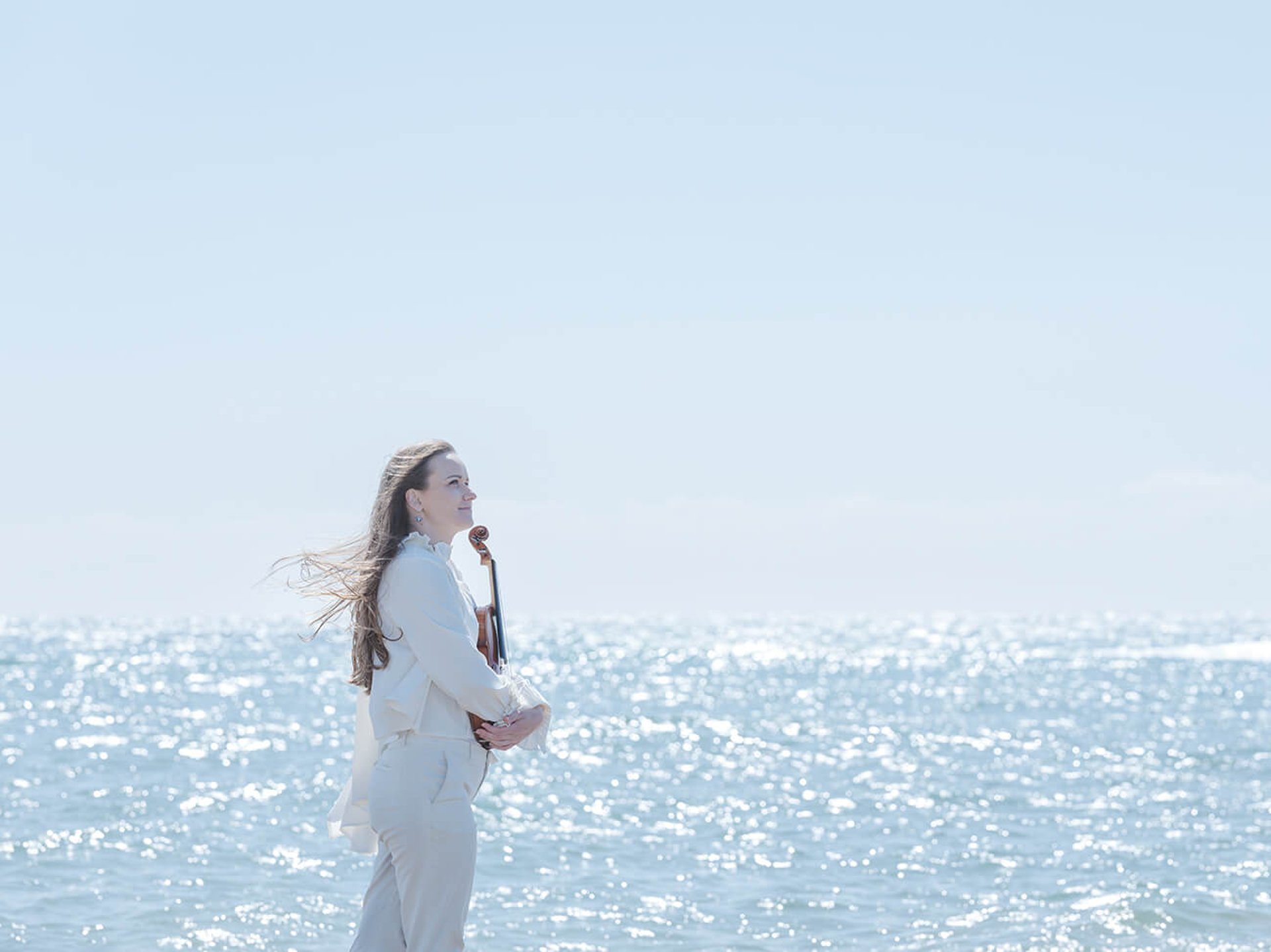 リトアニア人ヴァイオリニスト、ジドレが日本の海辺を晴れた日にヴァイオリンを持って歩いている