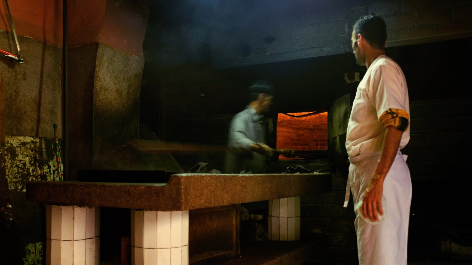Two men working in bakery with traditional wood fired oven