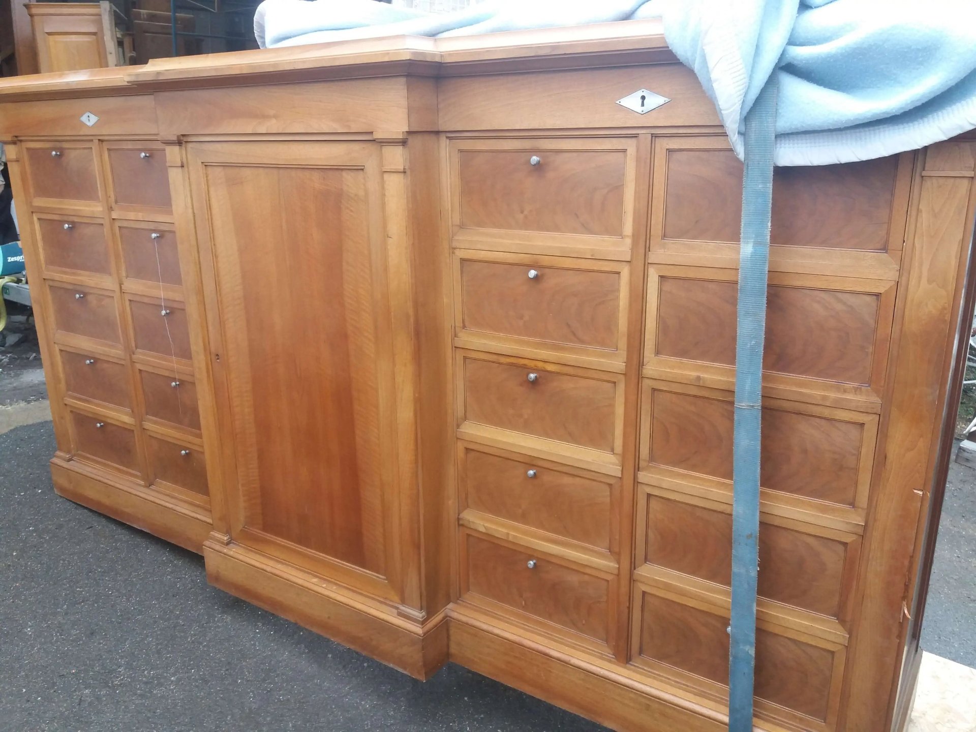 Brocante Lepeltier - Un buffet en bois à tiroirs, protégé d'un drap bleu.