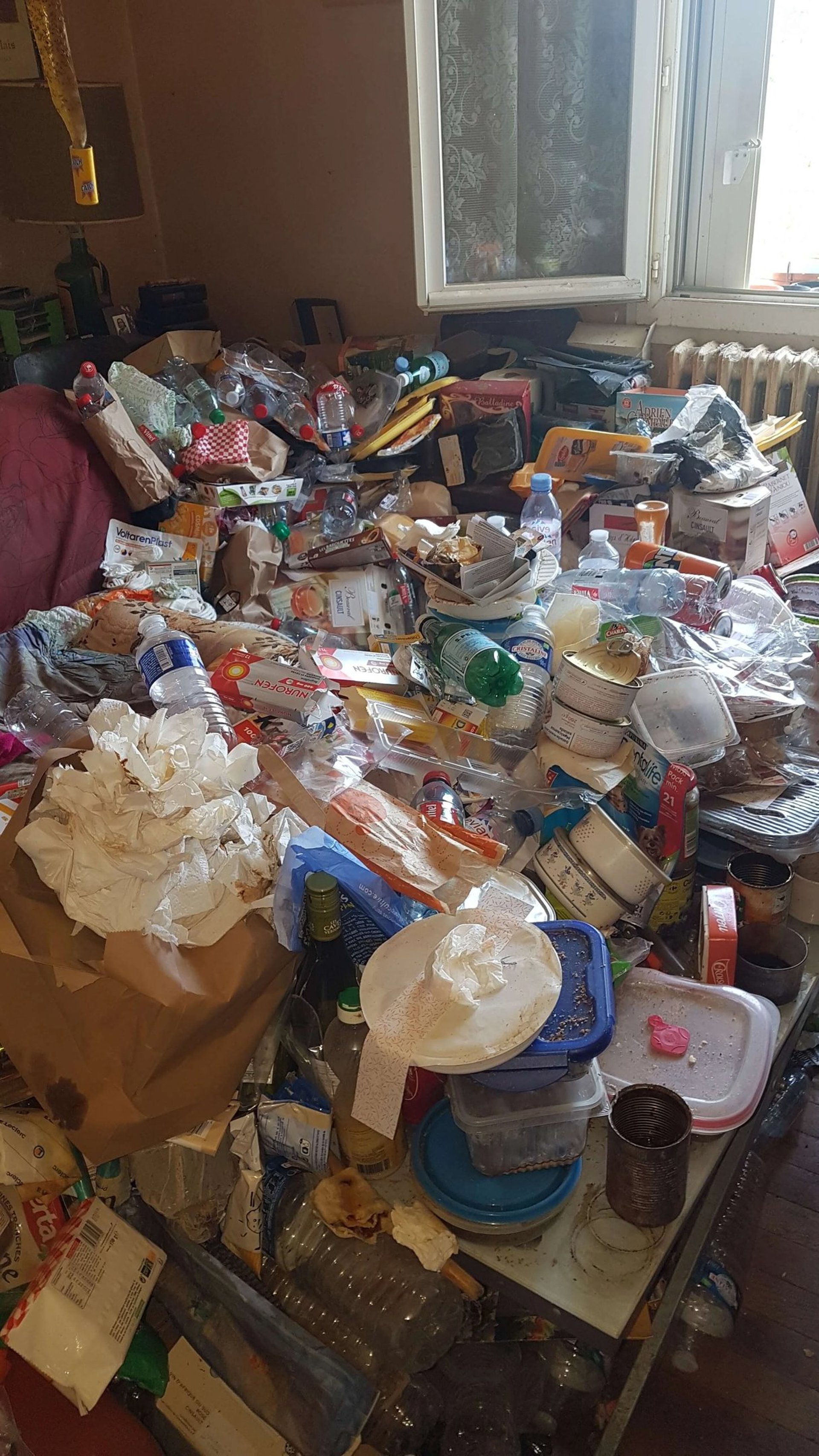 Débarras Lepeltier - Une chambre en désordre avec un lit et une table encombrée d'objets divers.