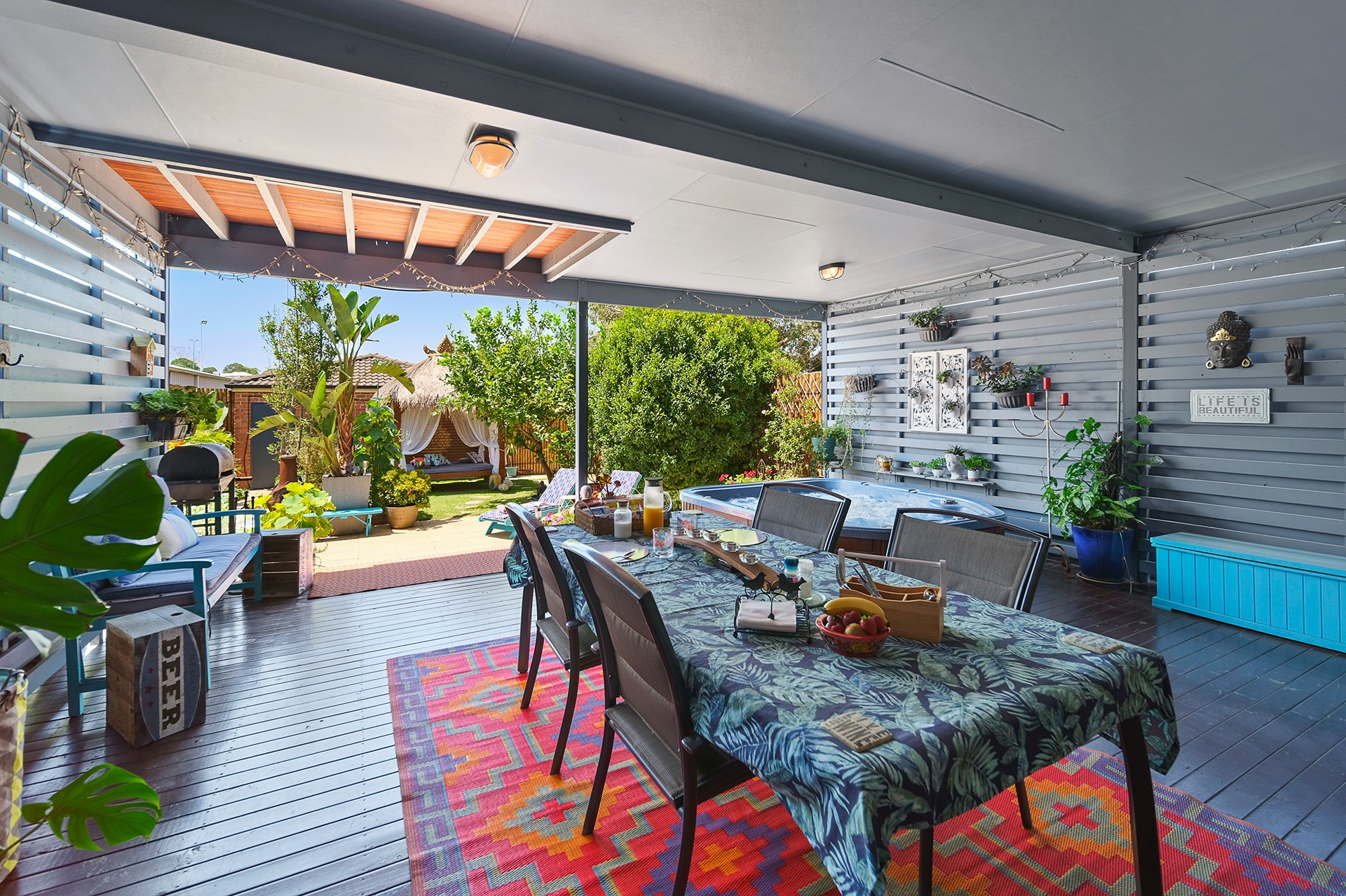 Outdoor patio at Marche Home Stay with a breakfast table, hot tub, lush garden, and cosy seating under string lights.