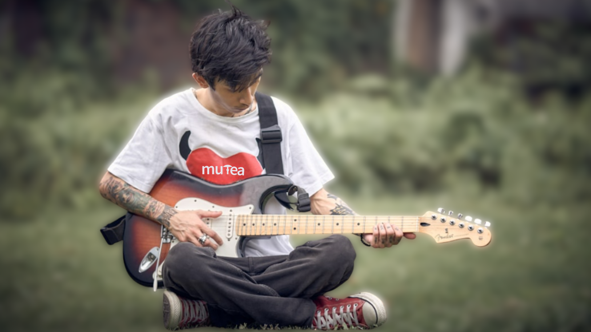 a young man sitting in the grass playing a guitar