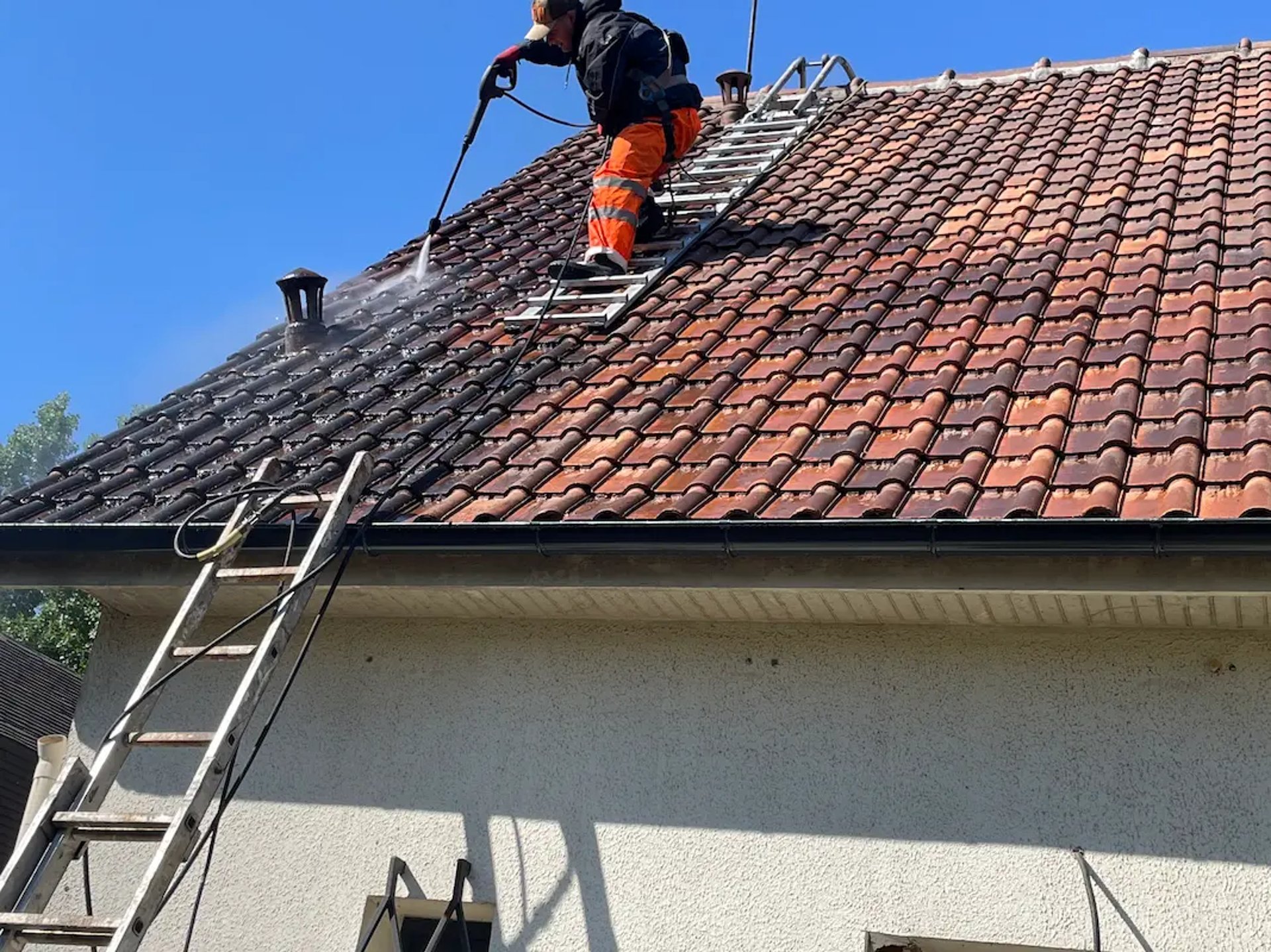 Artisan couvreur réalisant un nettoyage et démoussage haute pression sur une toiture en tuiles à Montmorency (95)