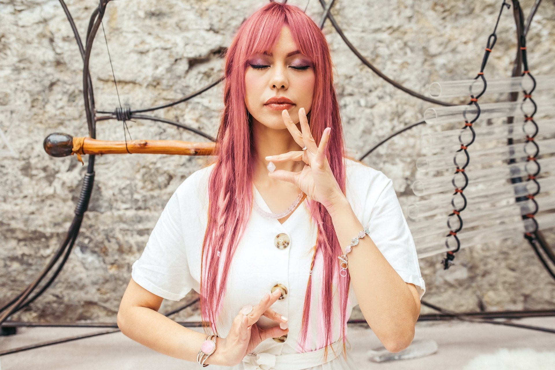 mujer de cabello rosa meditando en pose de mudra, con cristales de mudra