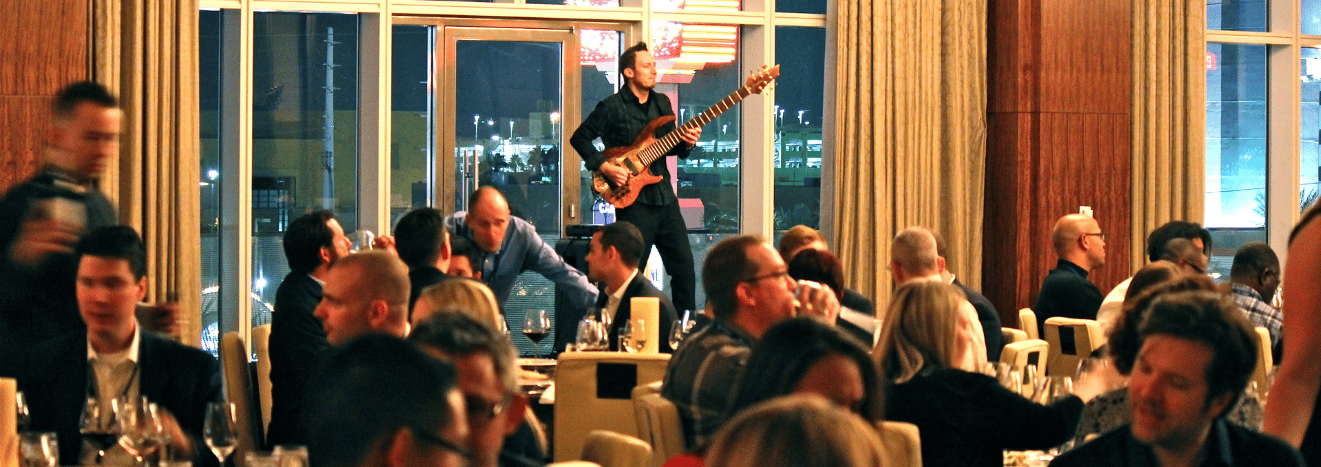 Jozef Bobula, solo bass player plays on an event stage in front of a crowded room of people dining at a corporate gathering.