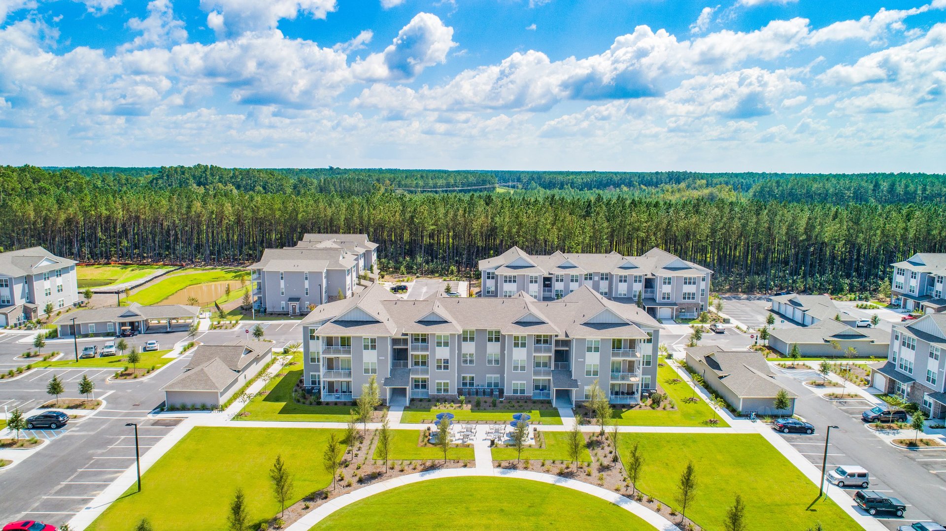 Ground-level view of outdoor patio seating with umbrellas between apartment buildings at Arrogate Village in Summerville, SC
