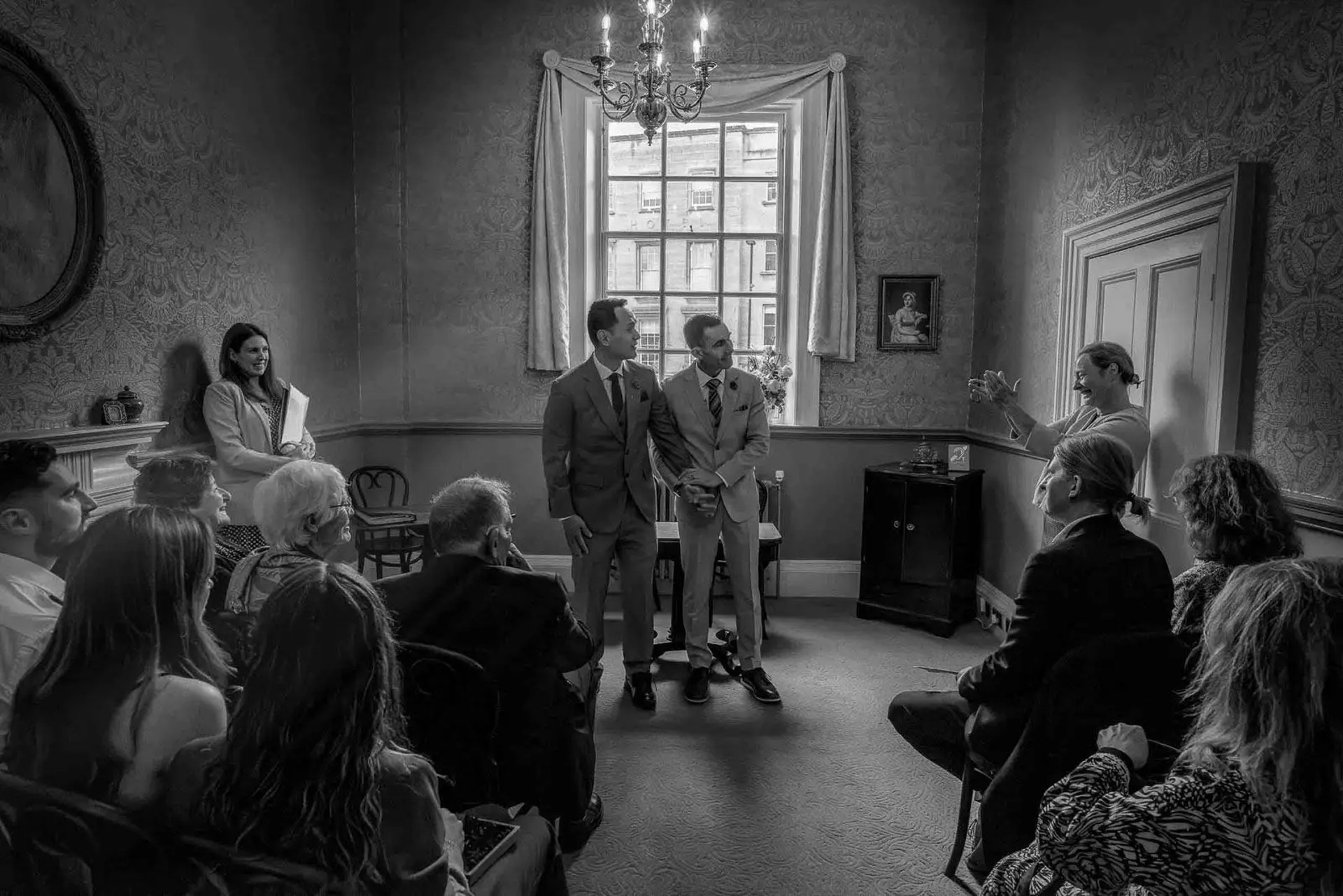 two grooms listening to their friend give a speech at their ceremony