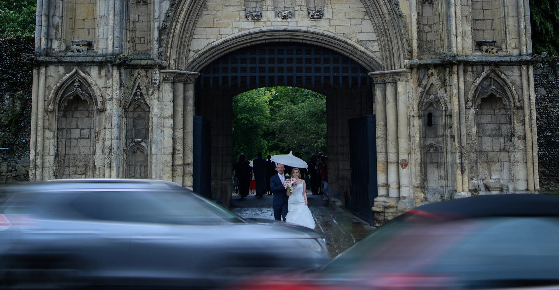 Wedding couple standing behind moving cars