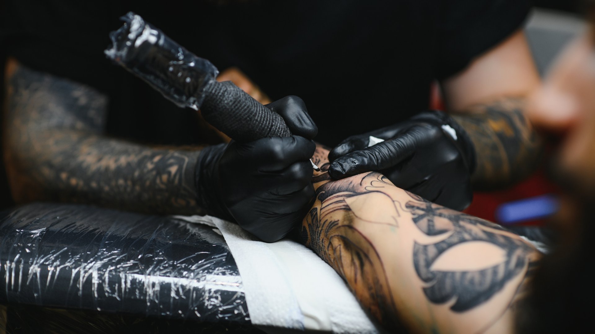 Tatuador realizando un tatuaje en negro en un brazo.