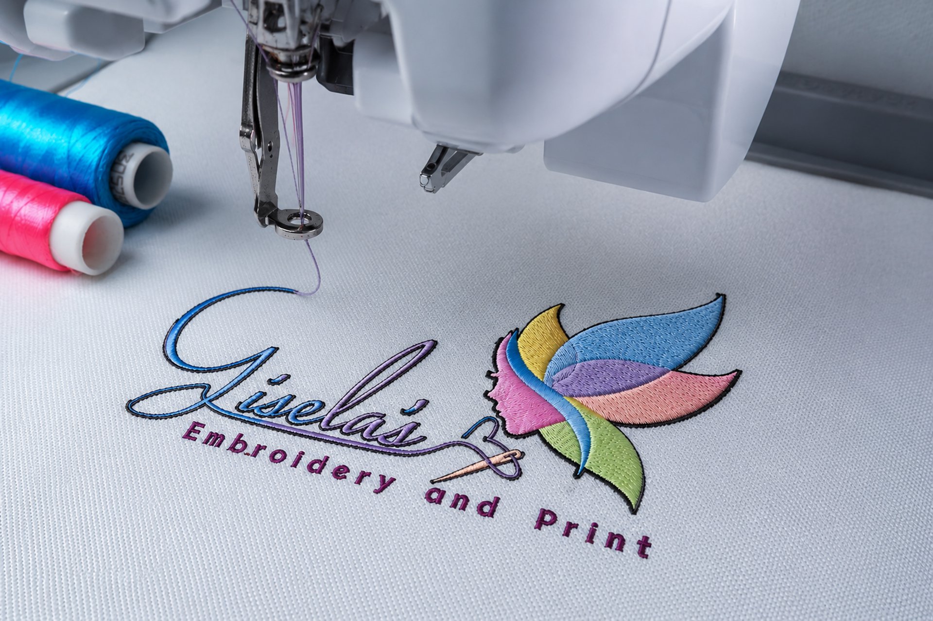 "Embroidery machine stitching the Gisela's Embroidery and Print logo onto white fabric."