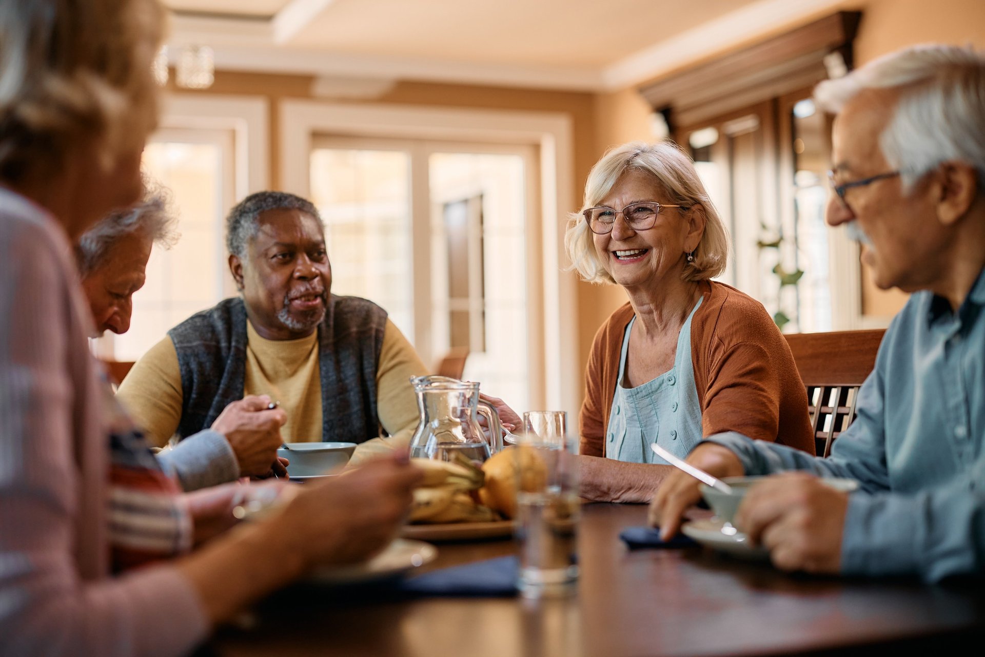 Group of elderly people sit at a table smiling and talking