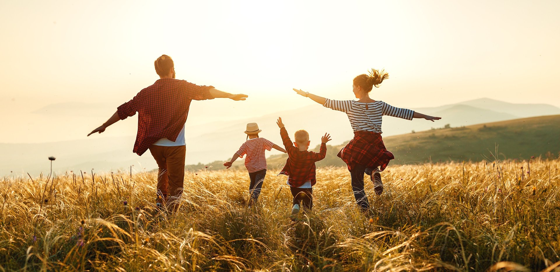 Family of a mother, father, and two children walking together happily through a field
