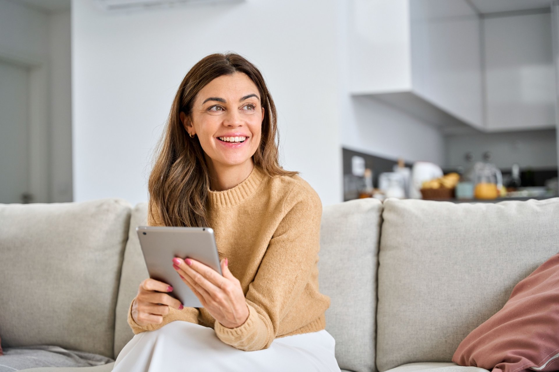 Woman smiles as she sits on couch holding tablet in her hands
