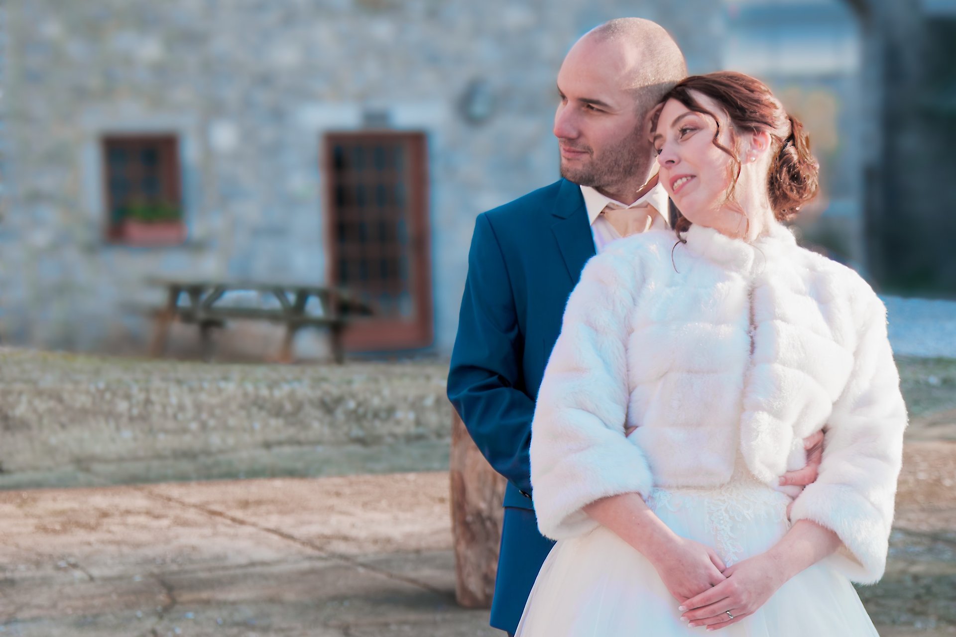 Une mariée vêtue d'un manteau de fourrure blanche et un marié en costume bleu posent