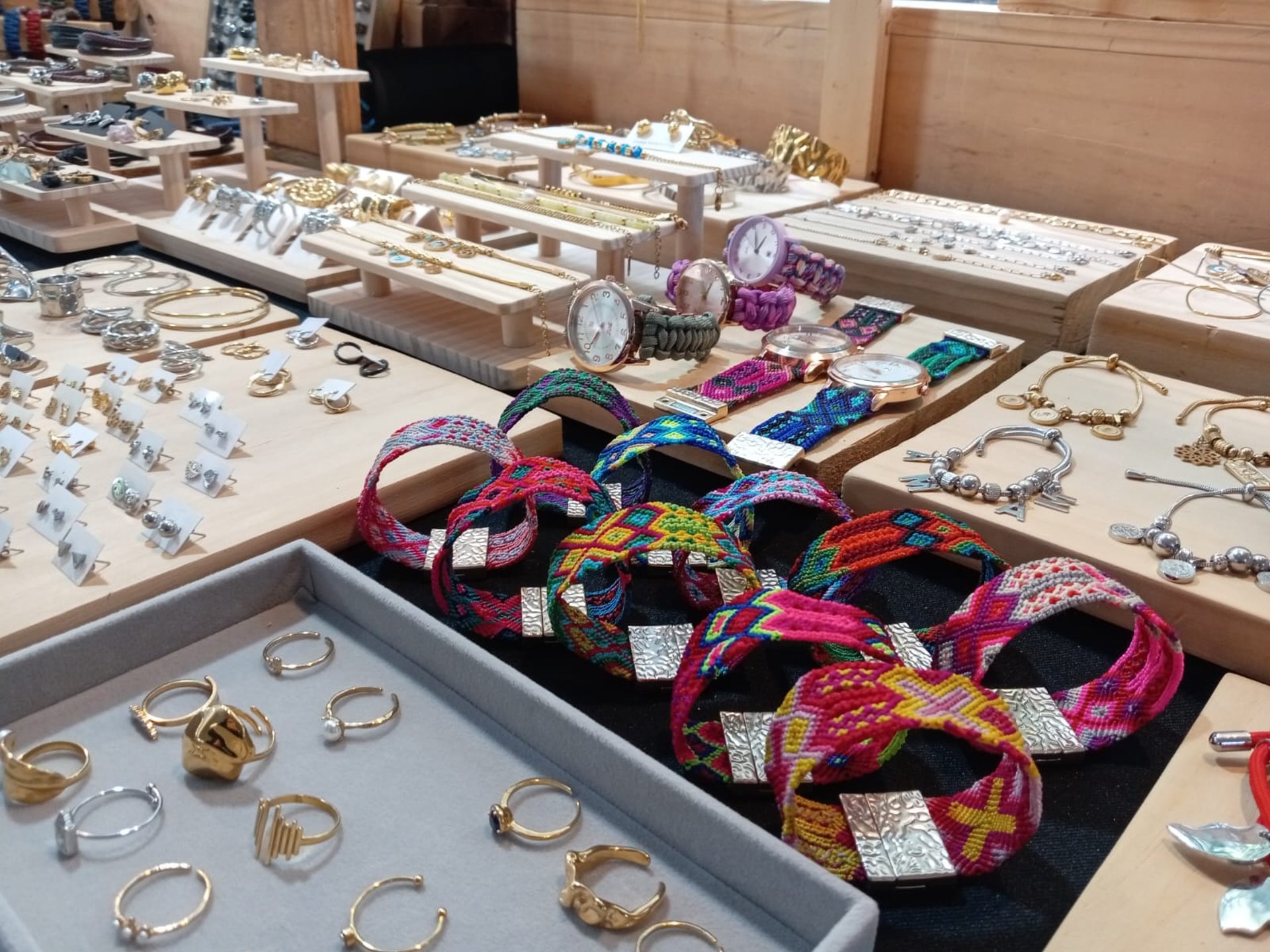 Exhibición de joyería artesanal con pulseras textiles, anillos y relojes en un bazar local