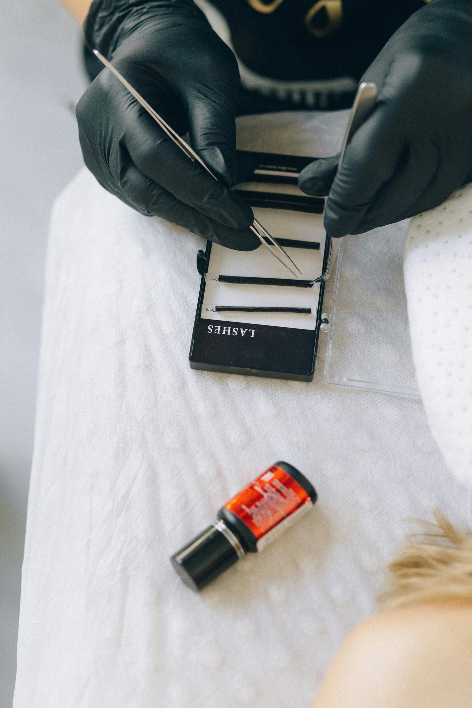persona tomando extensiones de pestañas de un blister y un adhesivo negro con rojo en la imagen