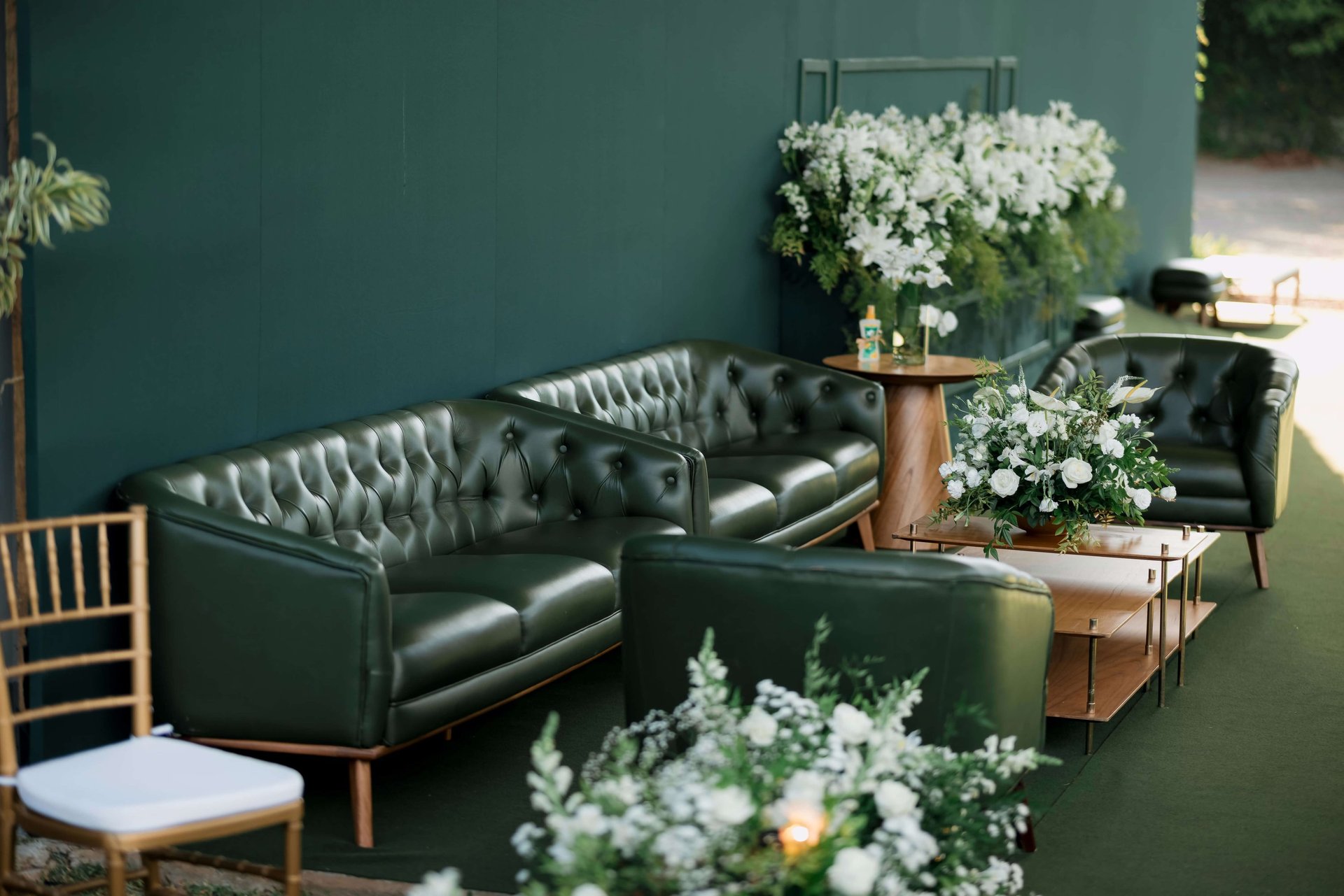 Elegant green tufted sofas with white floral arrangements.