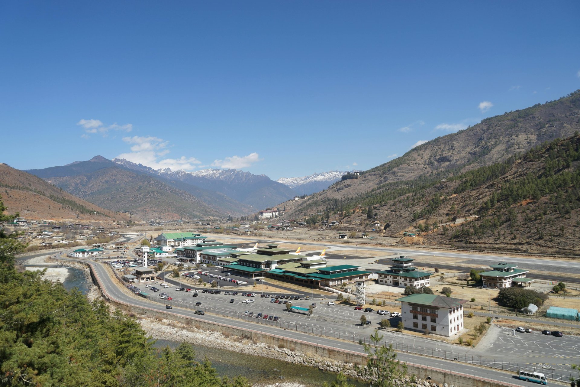 Airport buildings nestled by a river and mountains.