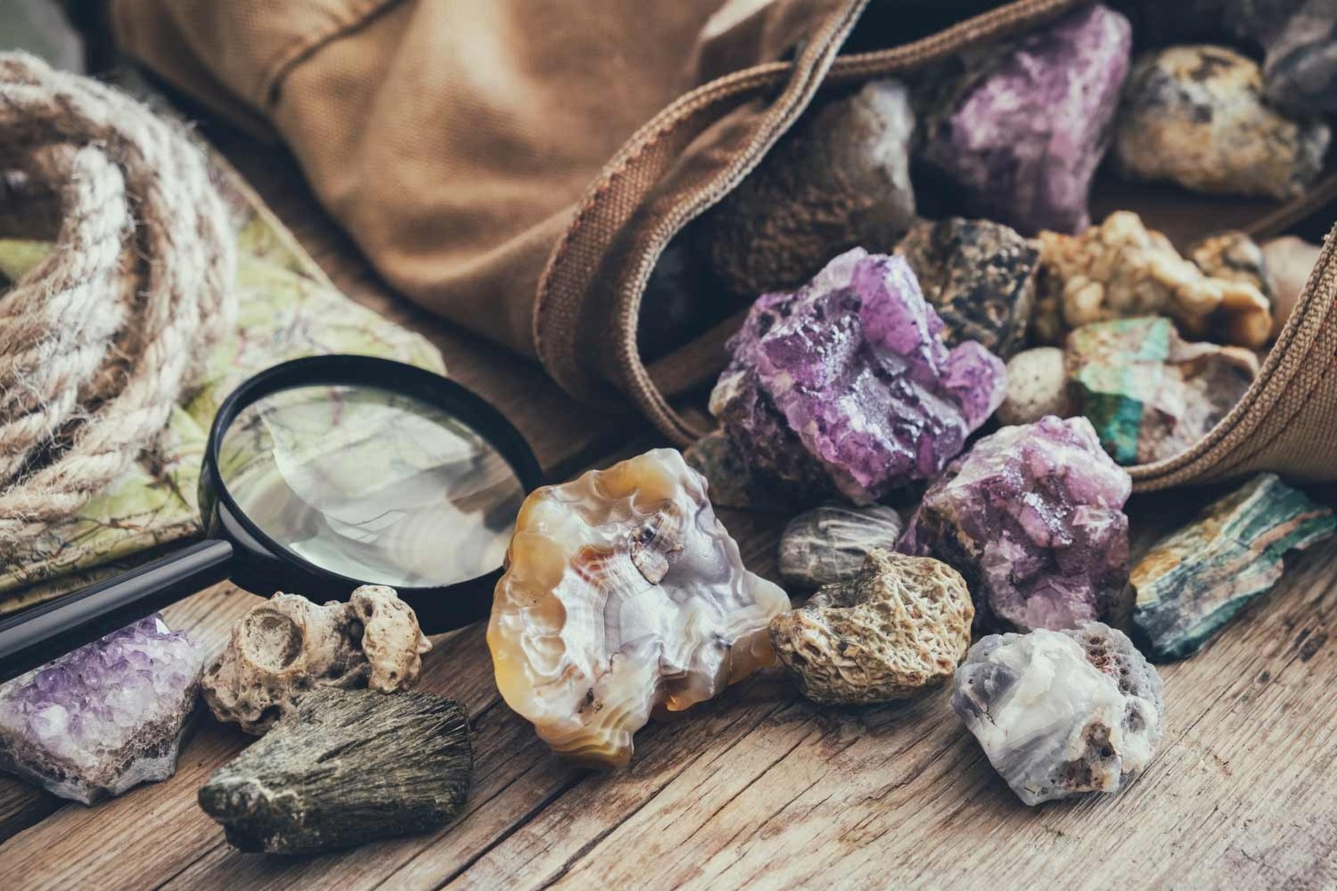 Piedras minerales irregulares y una lupa sobre mesa de madera