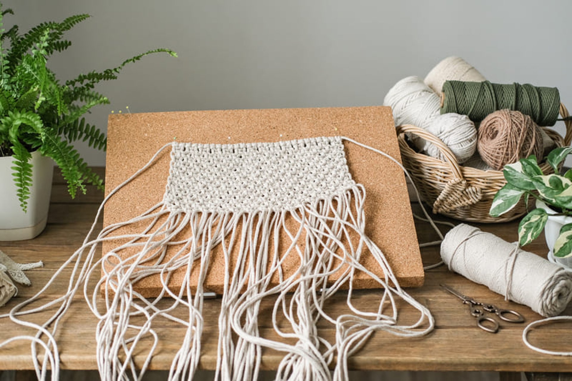 Fondo adorno de macrame hecho a mano en color blanco sobre mesa de trabajo con hilo de algodon de colores y tijeras