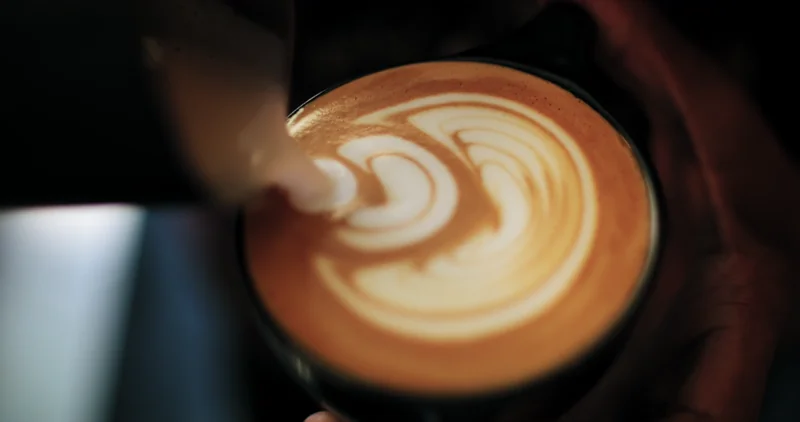 cup of coffee on saucer with teaspoon on pink tabletop