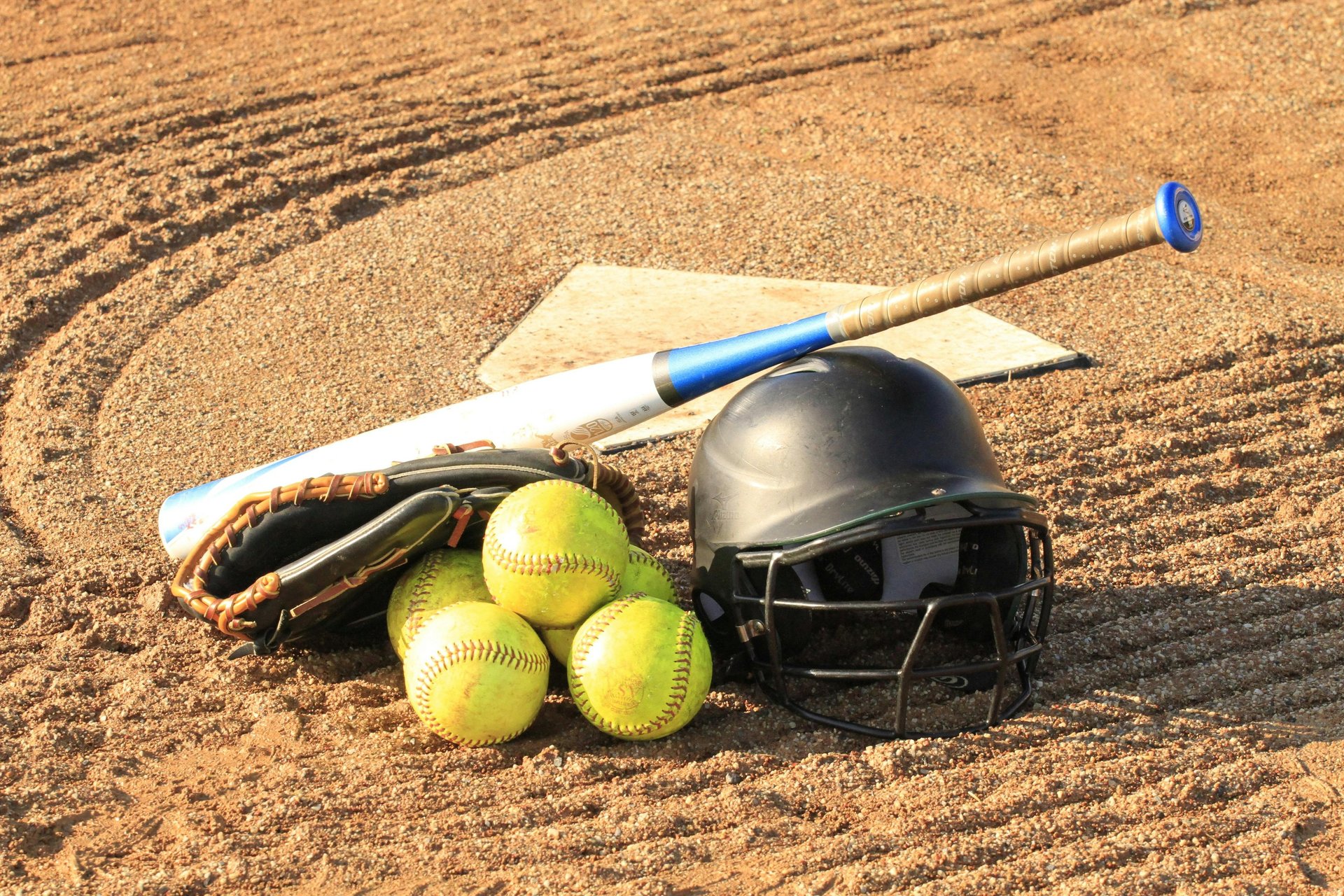 a baseball glove, catchers mitt, and helmet sit on a bench