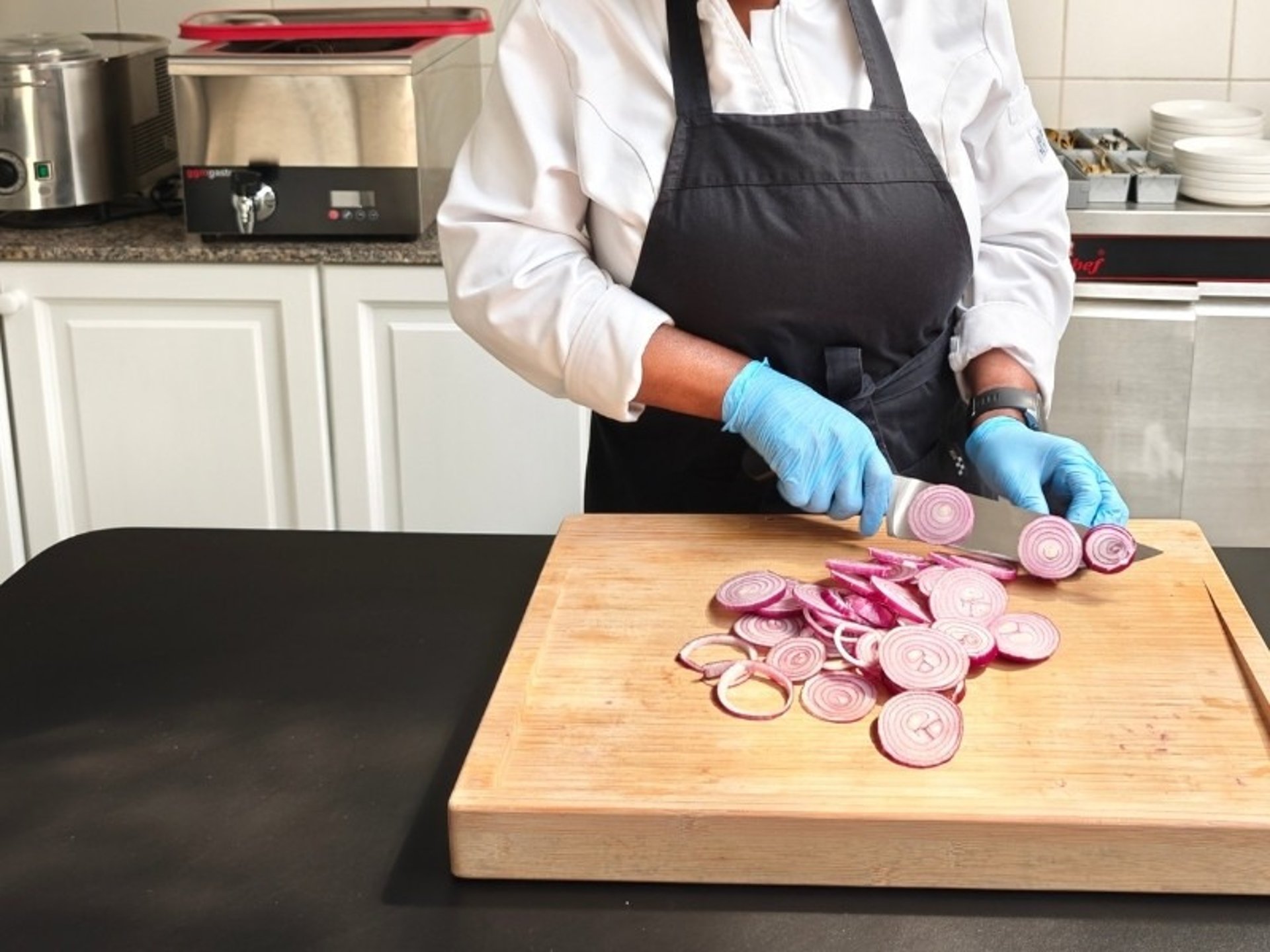 Chef Viviane slicing red onions on a bamboo cutting board in a professional kitchen — knife skills and kitchen technique