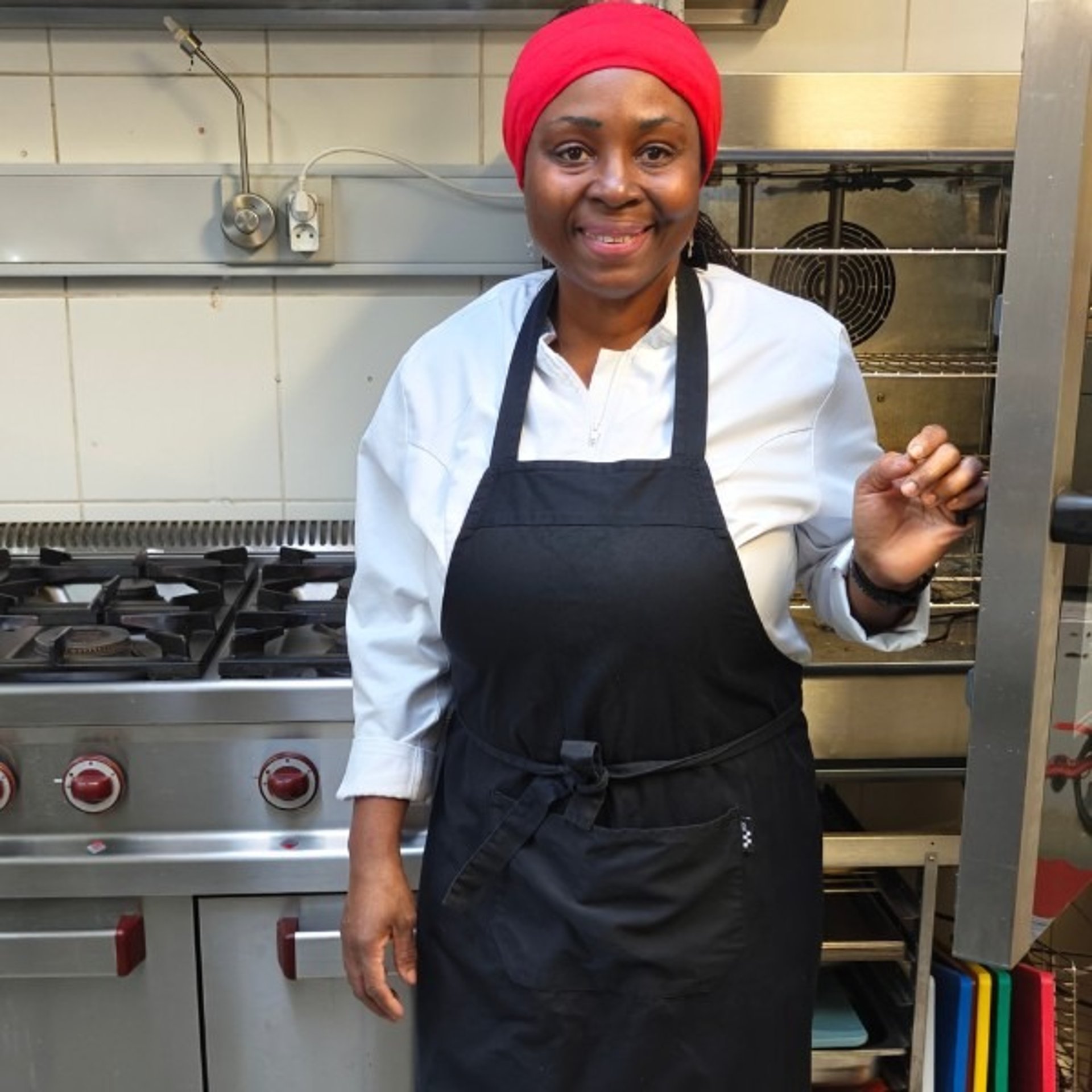 Chef Viviane Williams standing confidently beside a professional gas stove in her restaurant kitchen