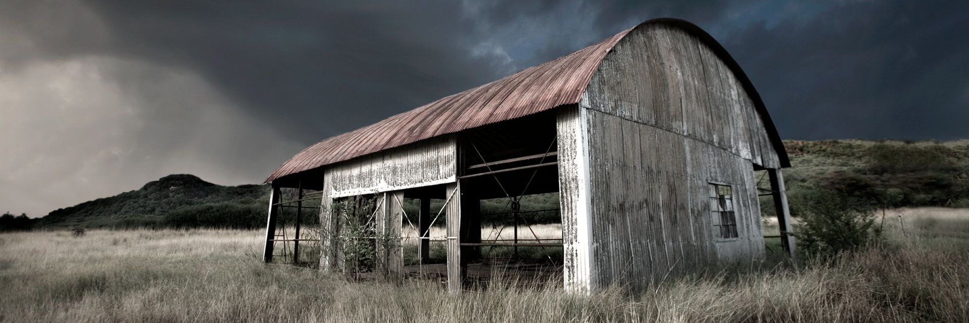 Weathered barn under a moody sky in an open field – fine art photograph by Martin Osner from the Abandoned Print Collection.