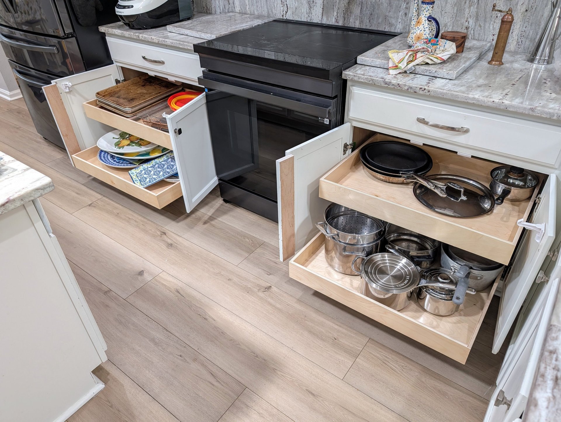 Two kitchen cabinets are open with glide out shelves extended out and filled with pots, pans and dishes. Better use of space!
