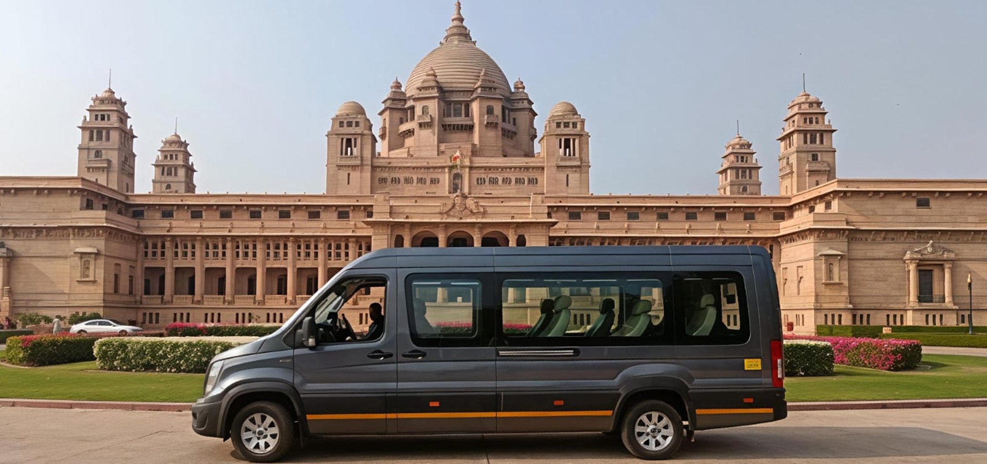 Three modern white Force Urbania vans parked in a sunny outdoor lot with trees and historic buildings in Delhi NCR