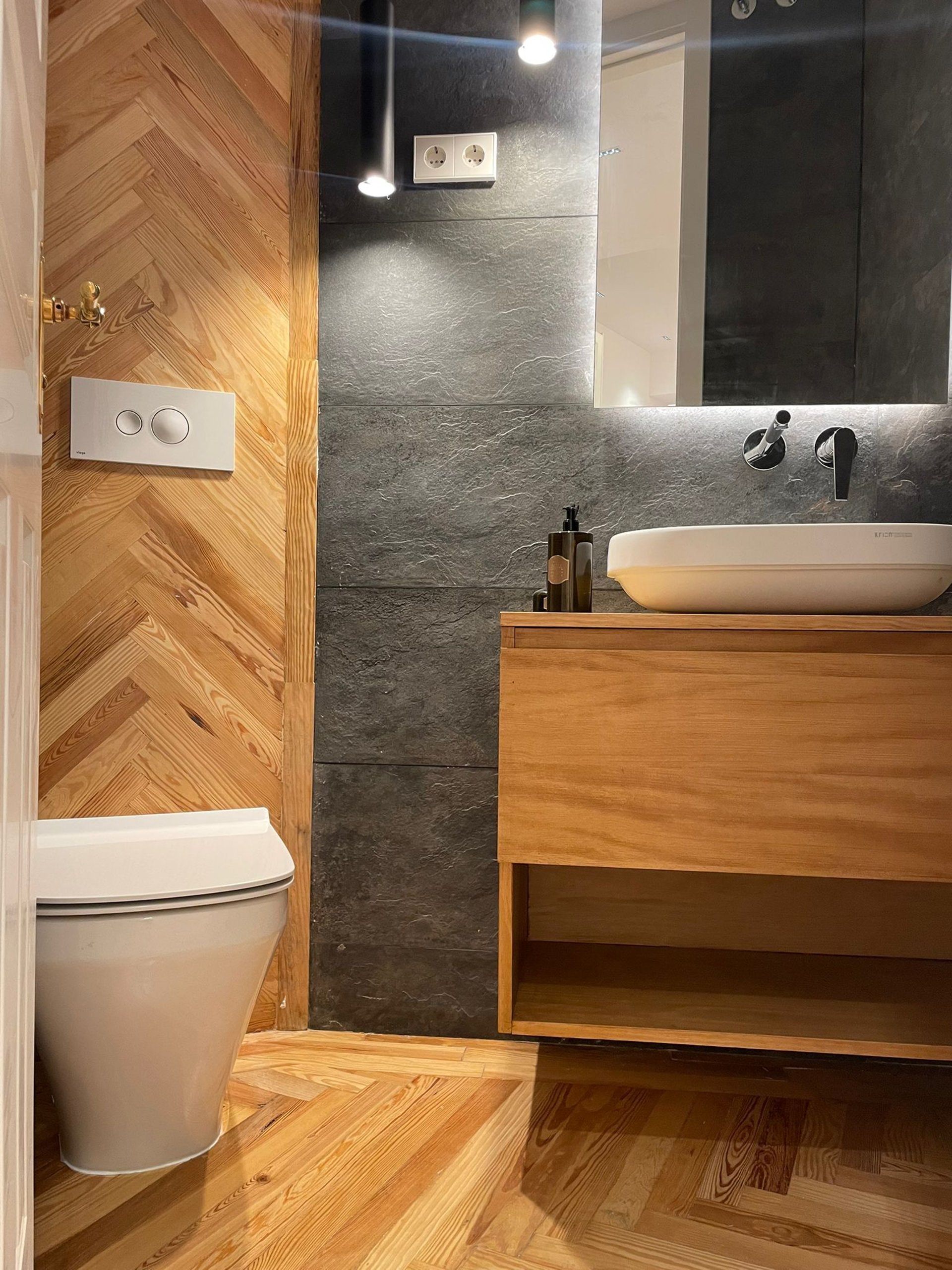 Baño moderno, madera espiga, lavabo y inodoro blanco.