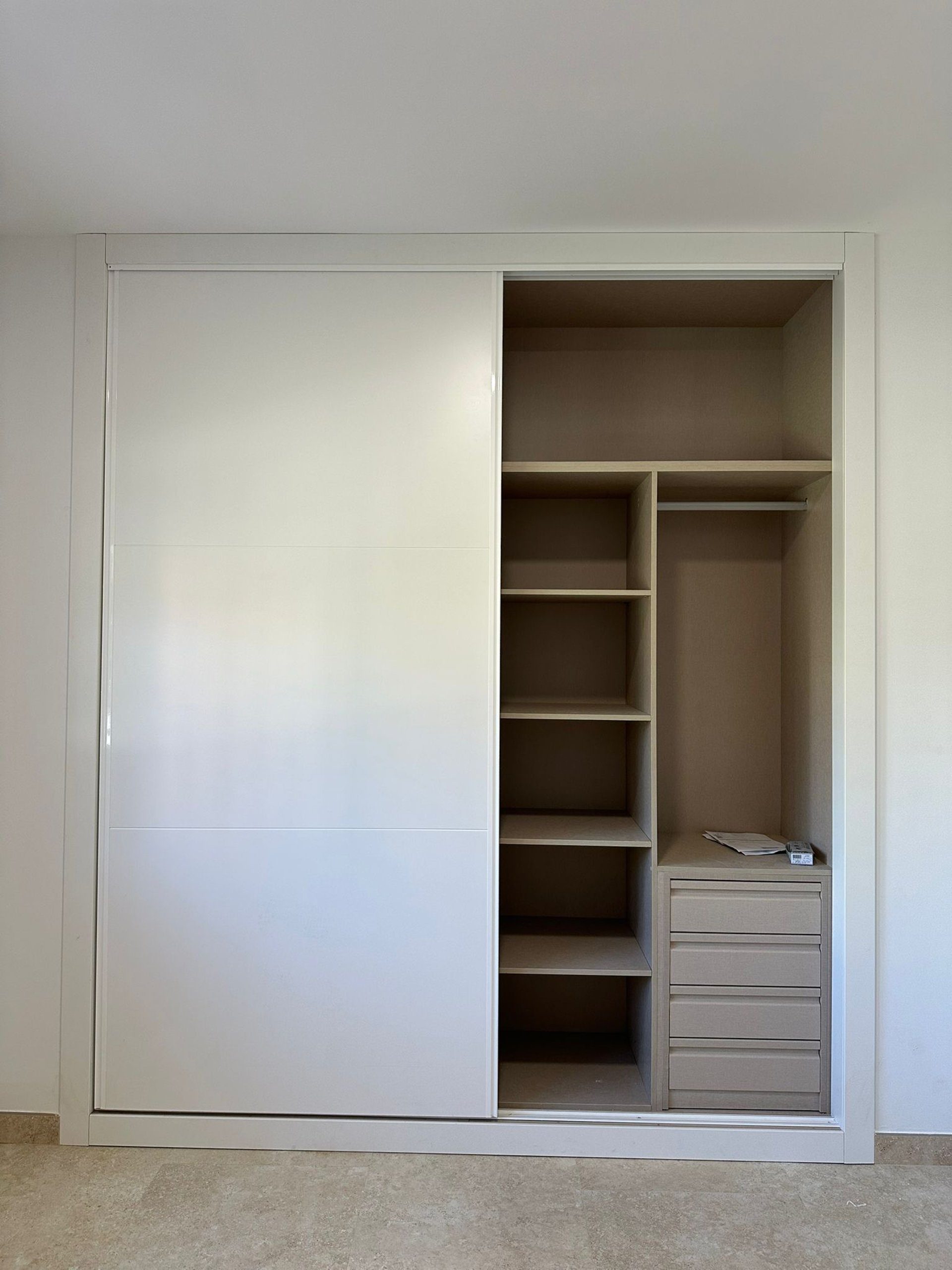 Armario blanco, puerta corredera abierta, estantes y cajones.