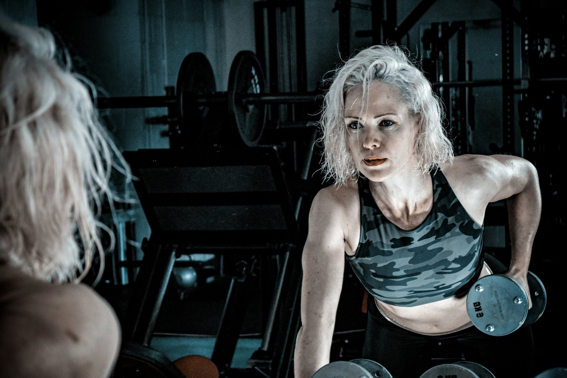 woman wearing black top top holding black dumbbells standing in front of mirror