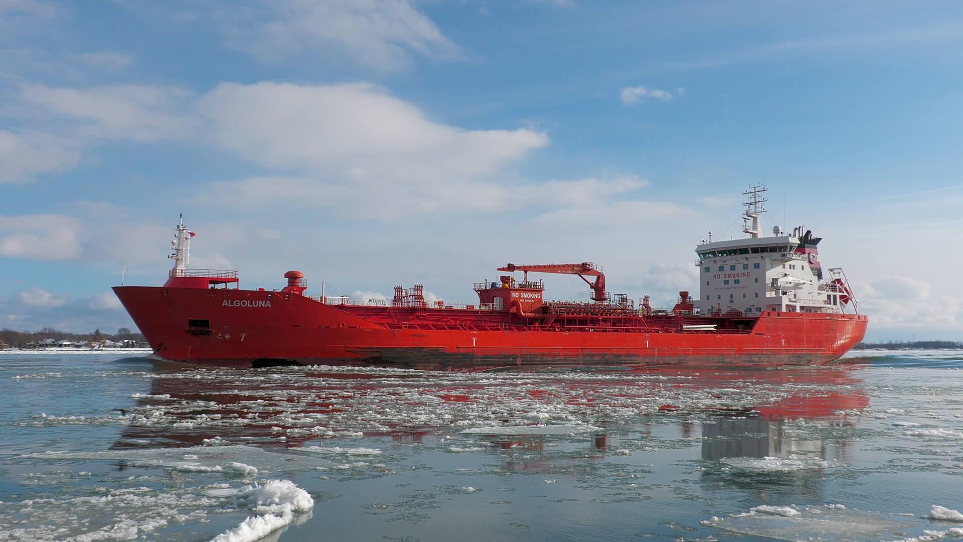 Left side view of tanker ship Algoluna on icy water, with a blue sky and sun reflecting off the side of the hull.