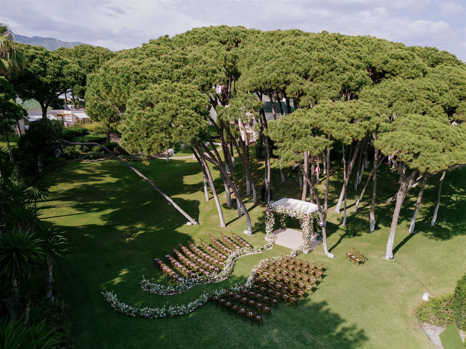 Wedding ceremony setup under tall pine trees at Villa El Rincon with floral arch and ocean views