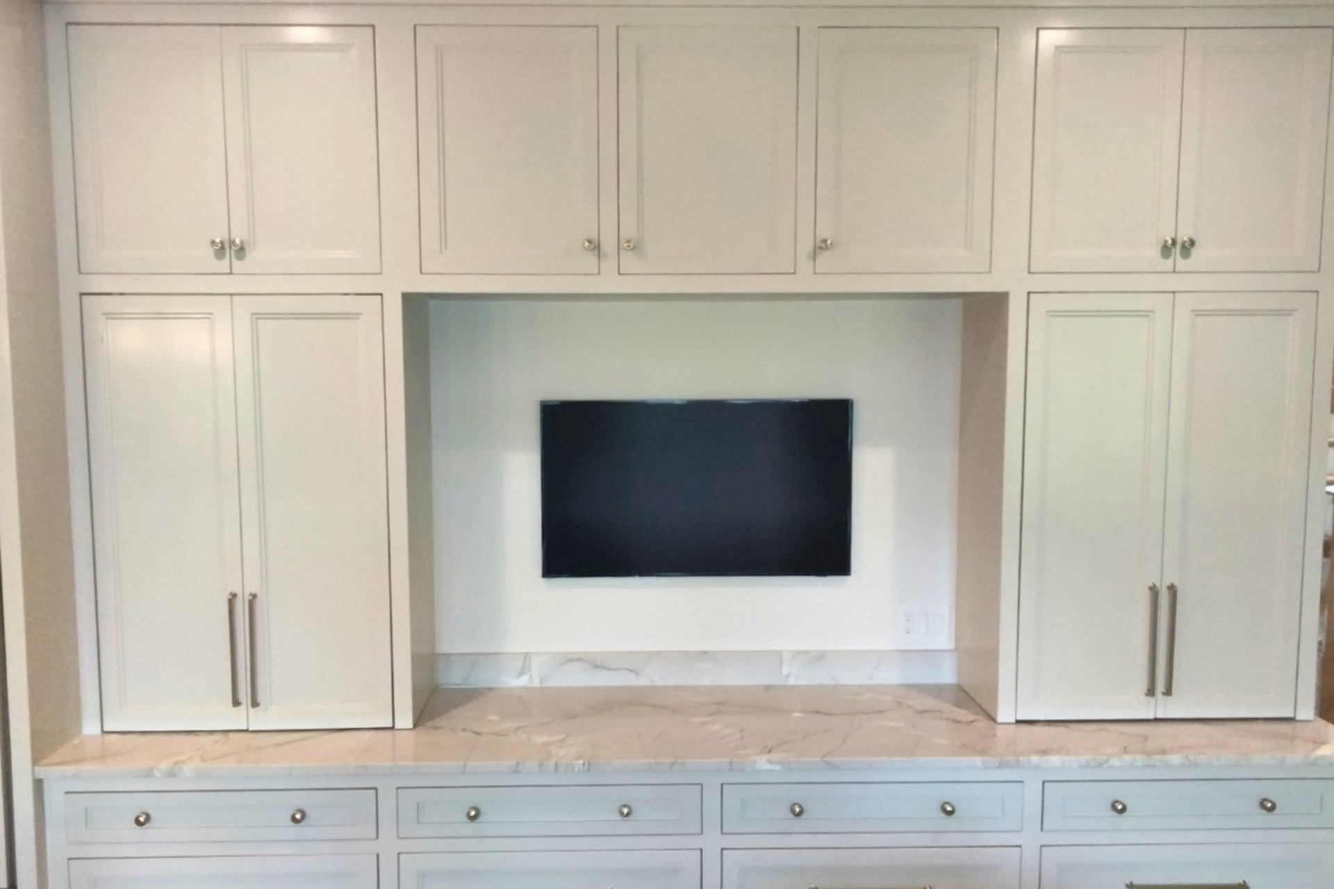 White built-in cabinets with stone countertop and TV niche