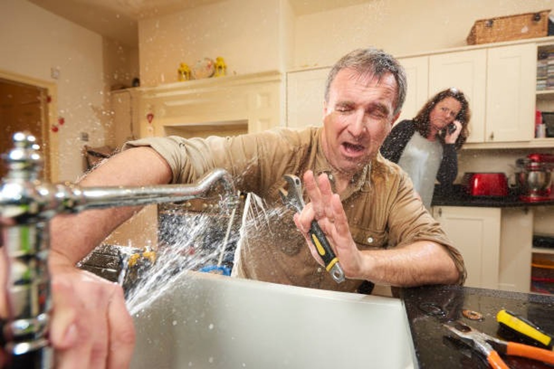 man getting sprayed n the face by the leak in his sink 