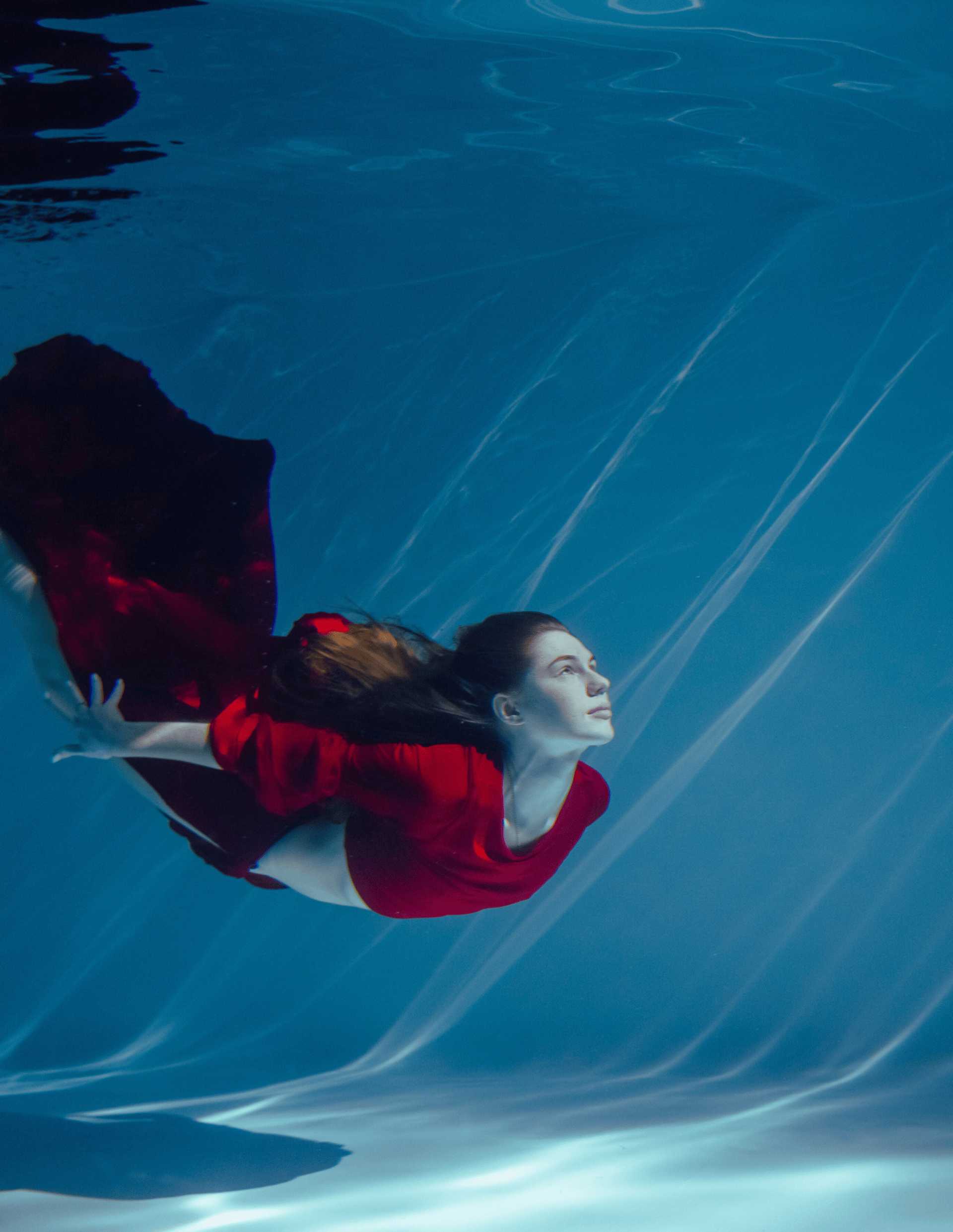 Empowered woman in red dress swimming underwater, symbolizing flowing success and freedom as a Phoenix Water Archetype