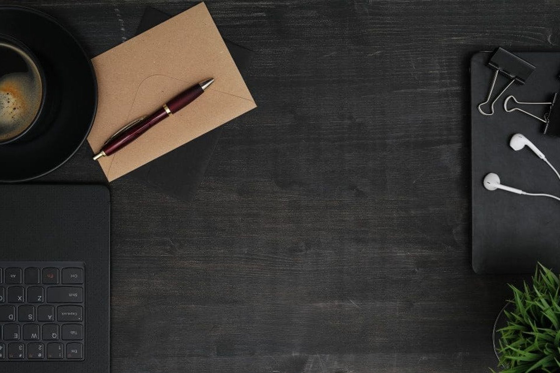 Vista superior de escritorio negro con café, sobre, bolígrafo, cuaderno y audífonos blancos