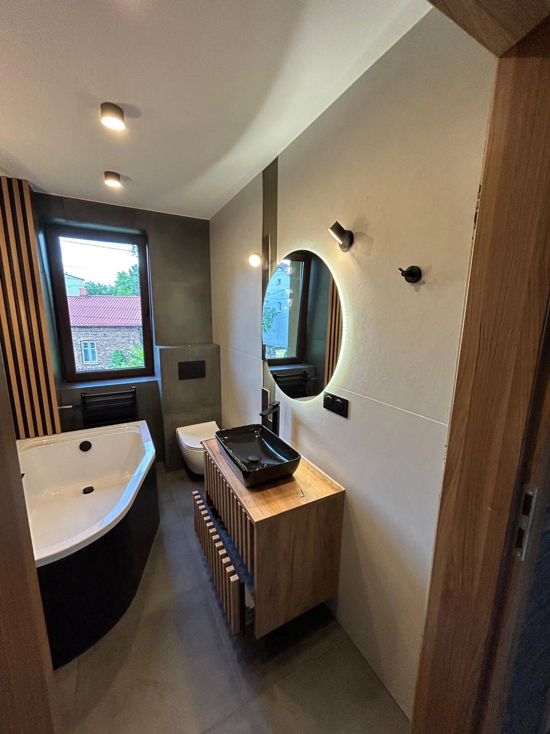 Łazienka w stylu loftowym z czarną umywalką, drewnianą szafką i wolnostojącą wanną.