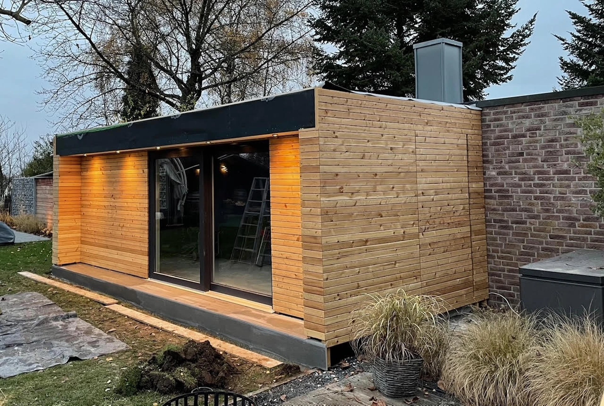 Wnętrze sauny z dużym oknem, drewniane ściany i sufit, podłoga z szarych płytek ceramicznych.