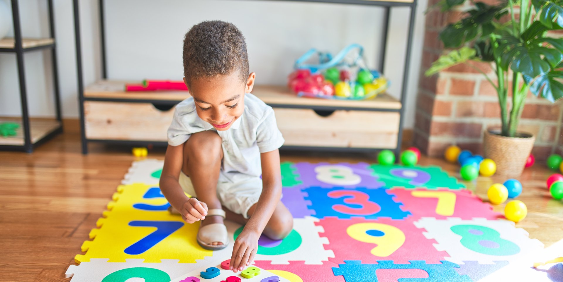 young boy playing with number blocks on a numbered mat on the floor