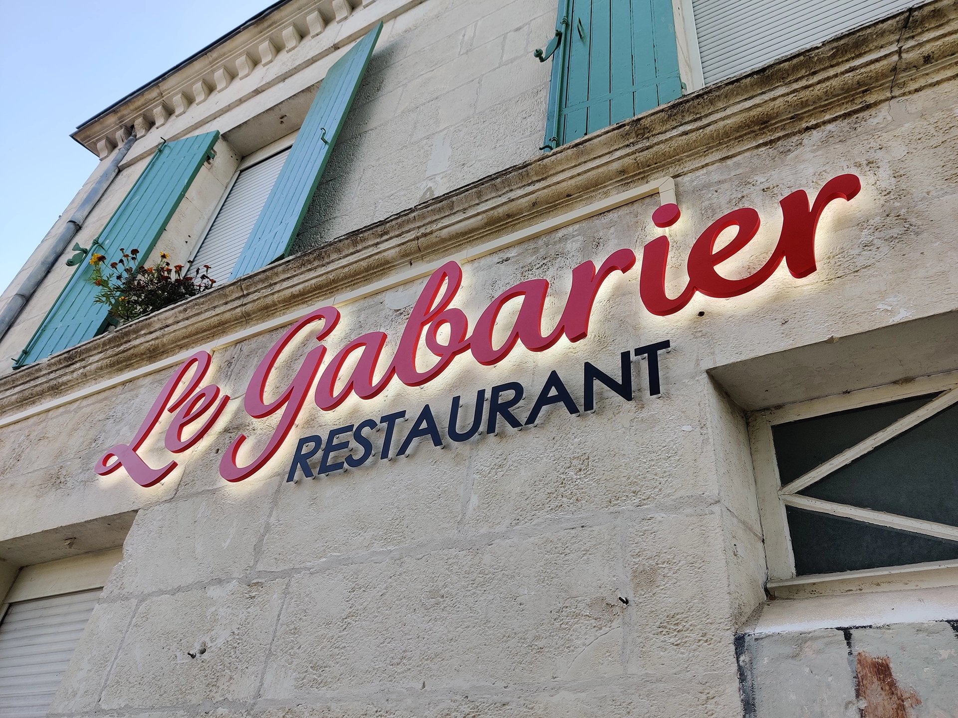 Façade du restaurant Le Gabarier avec son enseigne lumineuse rouge et noire sur mur en pierre blanche.